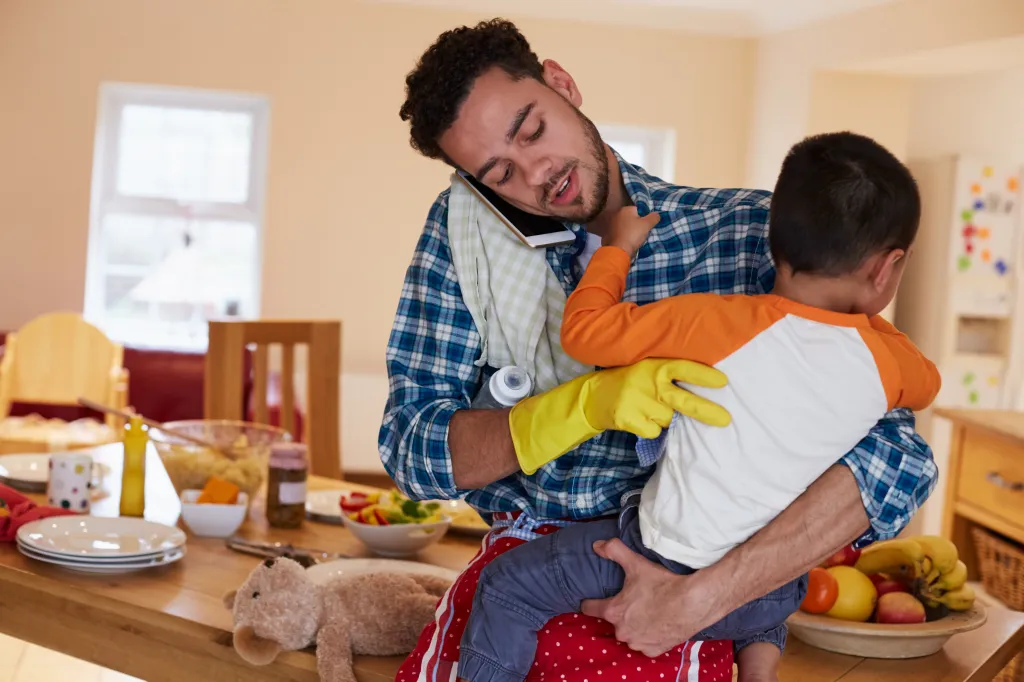 A father looking busy in the house holding a kid.