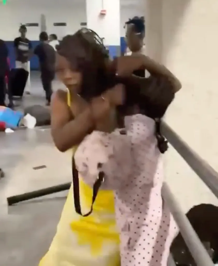 Two women fighting, one in a yellow dress and one in a polka dot outfit, in a public area.