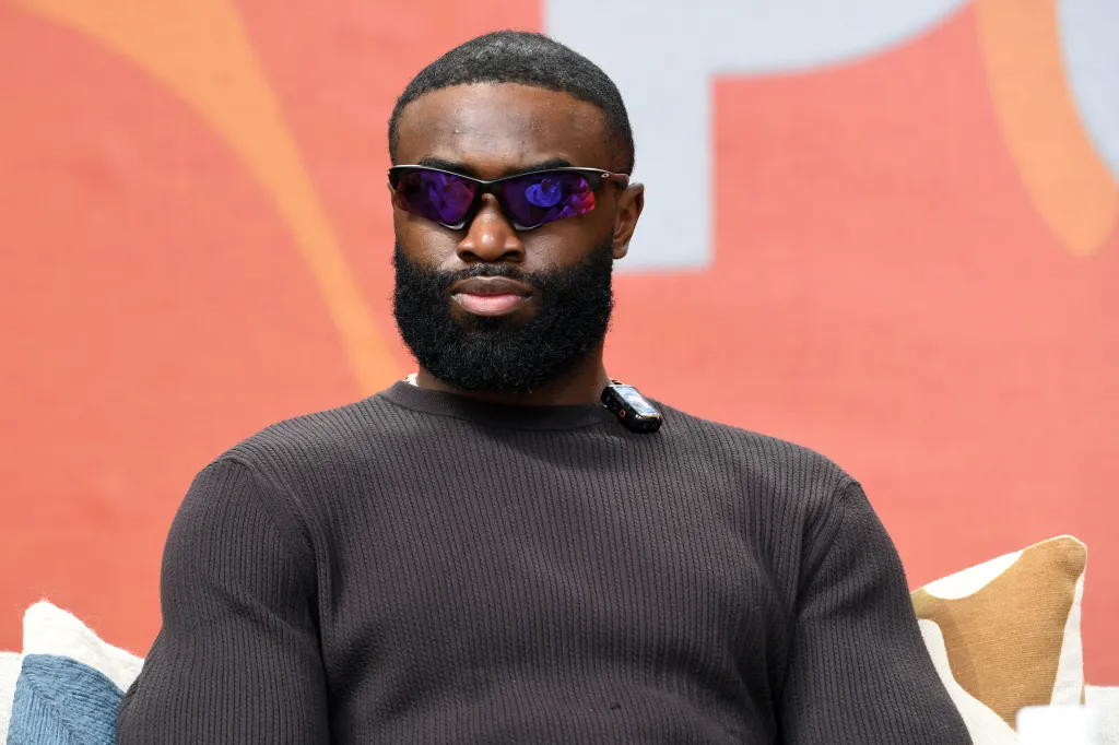 Jaylen Brown, NBA champion, in a close-up shot, wearing a dark brown ribbed sweater and dark sunglasses.