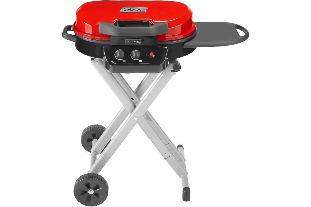A red Coleman portable grill with a side table, controls, and wheels on a white background.