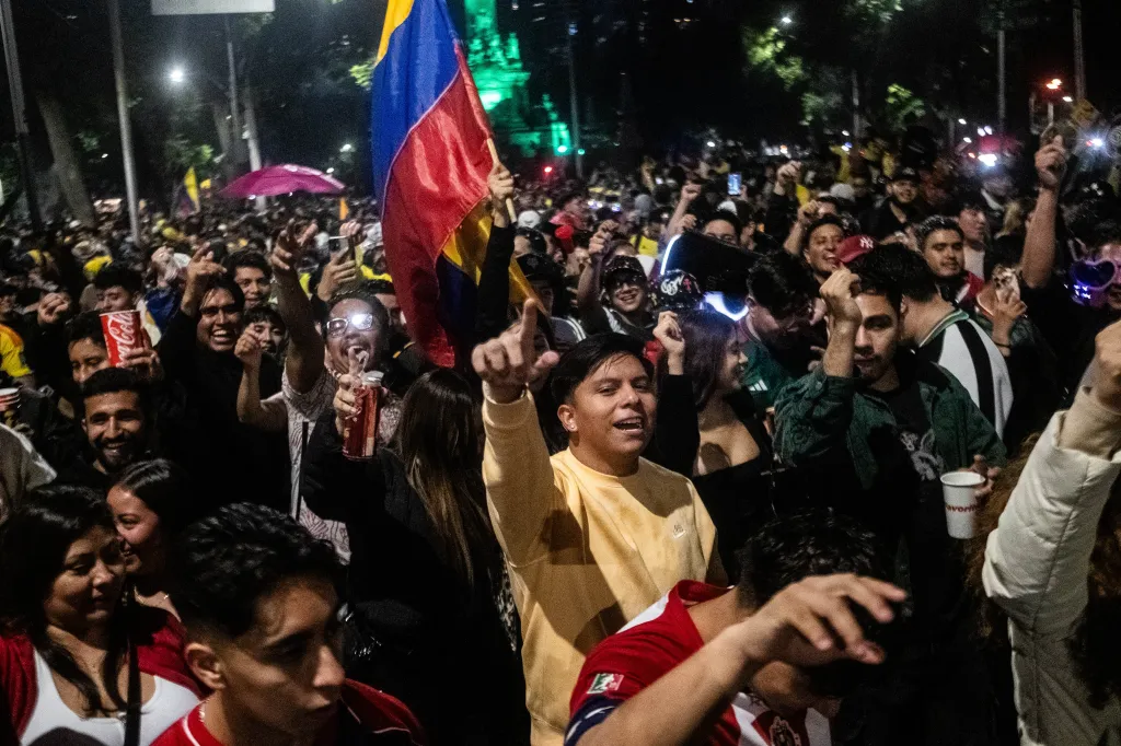 Colombian soccer fans celebrating their team's victory at night, with one fan holding a Colombian flag.