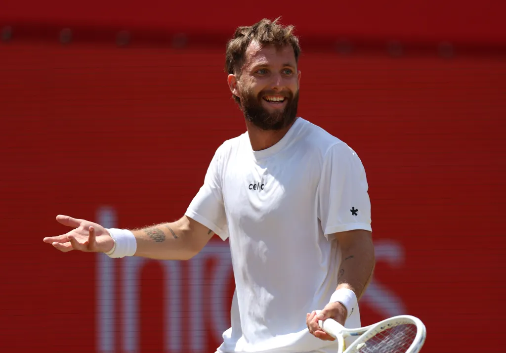 Tennis player Corentin Moutet in a white shirt and wristband, smiling and holding a racket.