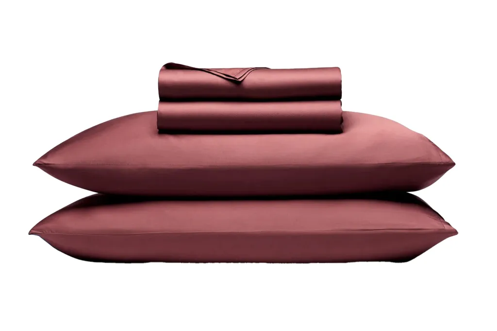 Stack of two maroon pillows with two folded maroon sheets on top.