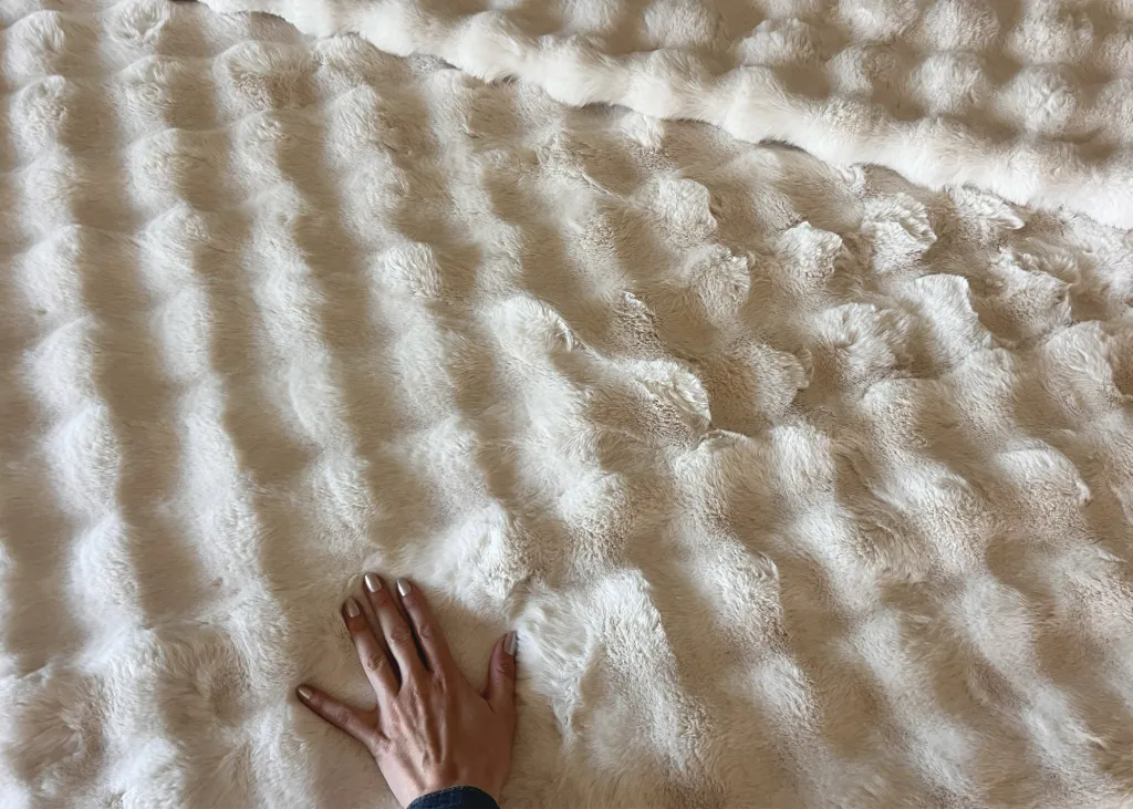 Hand resting on a plush, cream-colored blanket with a wavy texture.