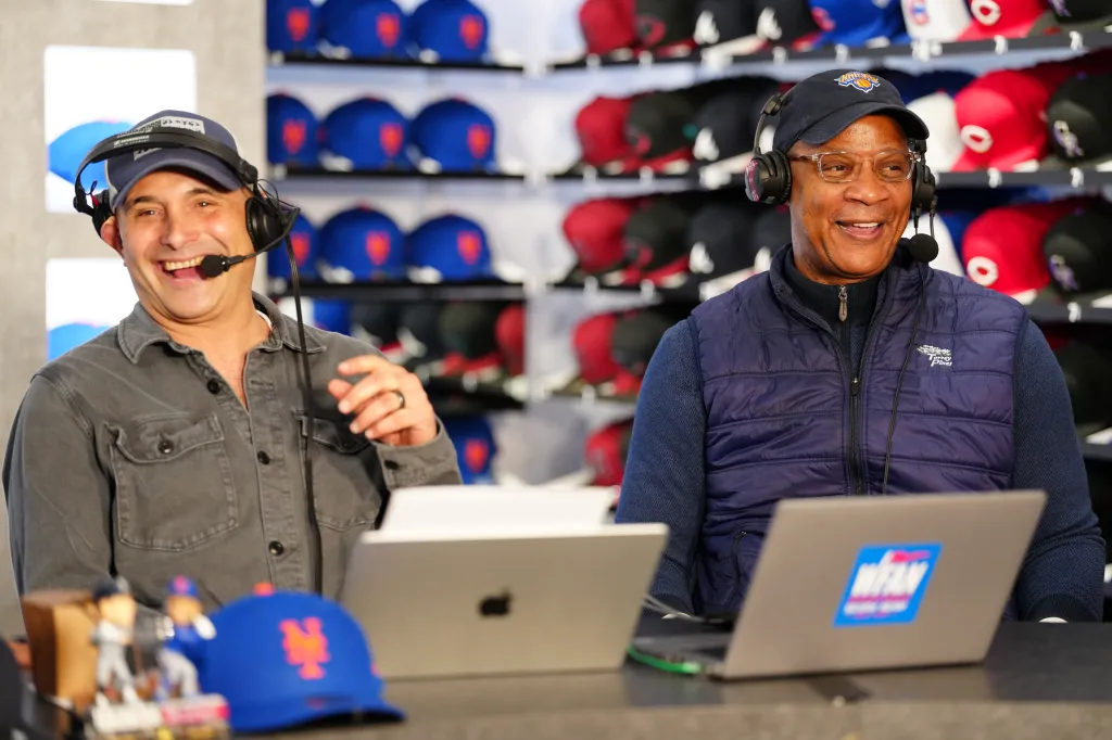 Two men in headsets broadcasting the WFAN Subway Series with laptops and baseball caps.