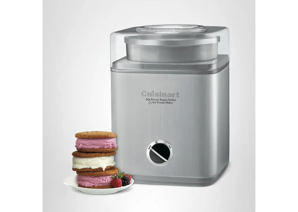 A Cuisinart ice cream maker next to a stack of ice cream sandwiches on a plate with berries.