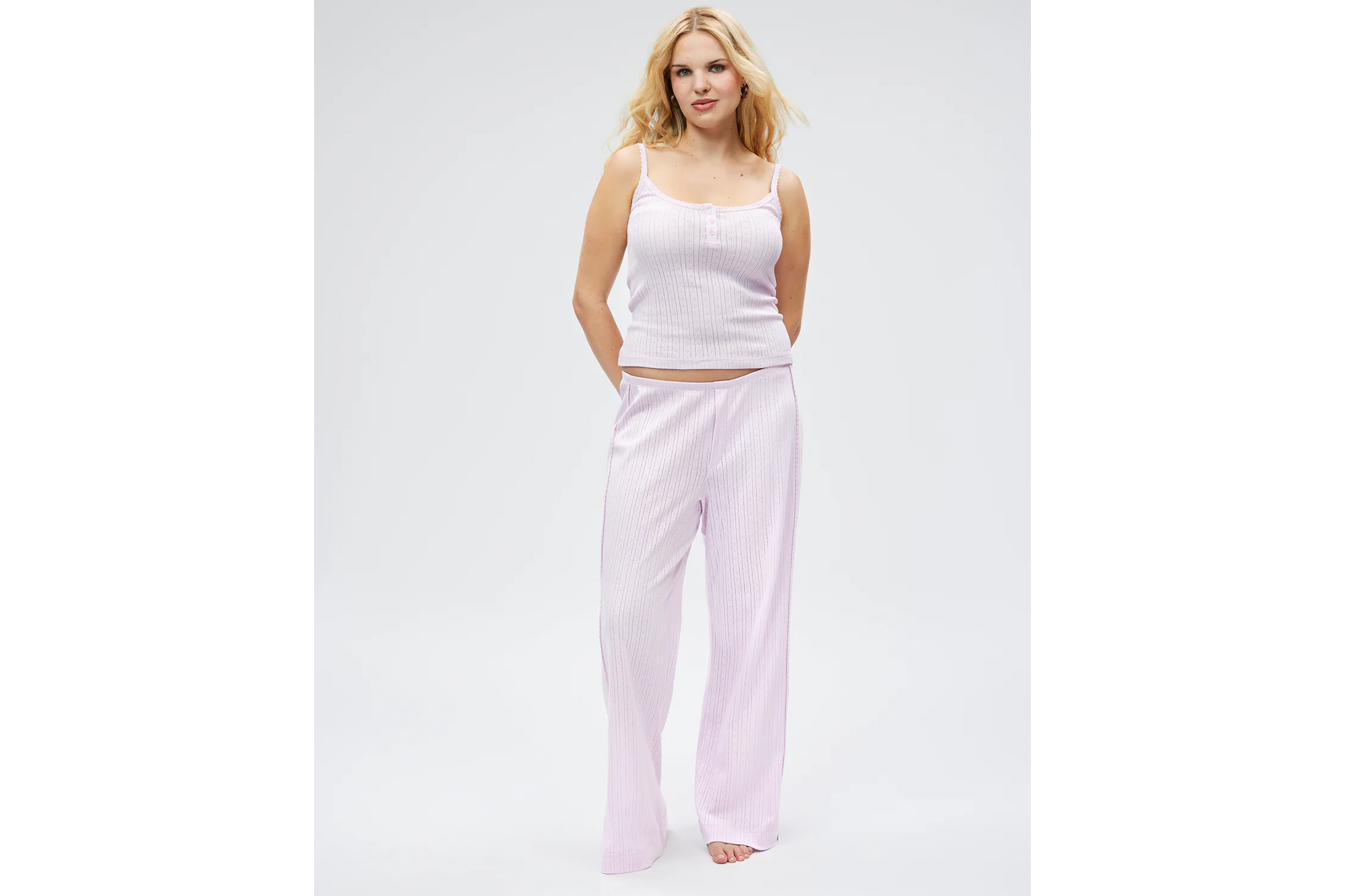 A woman modeling light purple pajamas with vertical stripes, featuring a tank top and wide-leg pants.