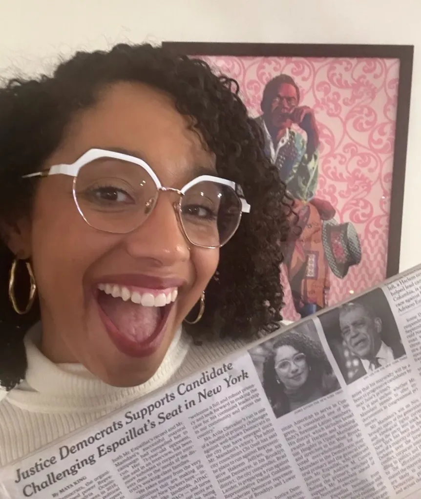 Darializa Avila Chevalier, a democratic socialist candidate, smiles while holding a newspaper featuring her candidacy.
