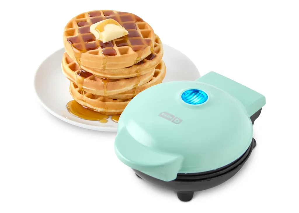 A Dash mini waffle maker in mint green with a stack of waffles on a white plate.