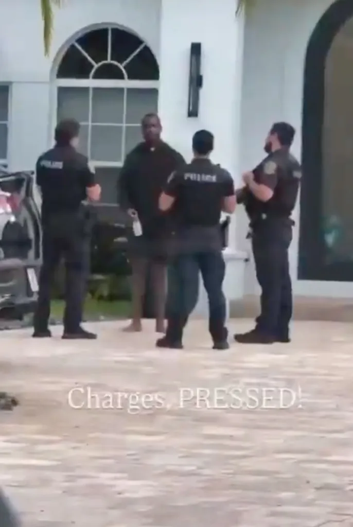 A man in dark clothing speaking with three police officers in uniform outside a white building.