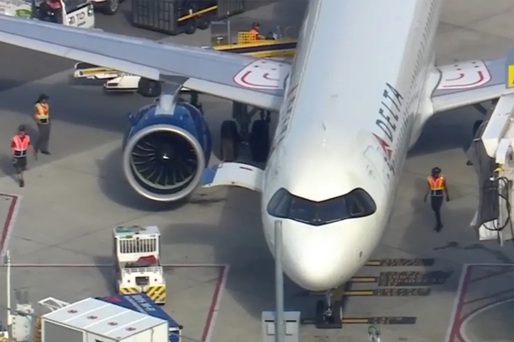 Aerial view of a Delta airplane on an airport tarmac, with airport staff nearby.
