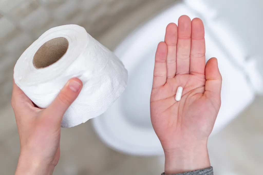 Hands holding toilet paper and a pill, symbolizing diarrhea treatment.