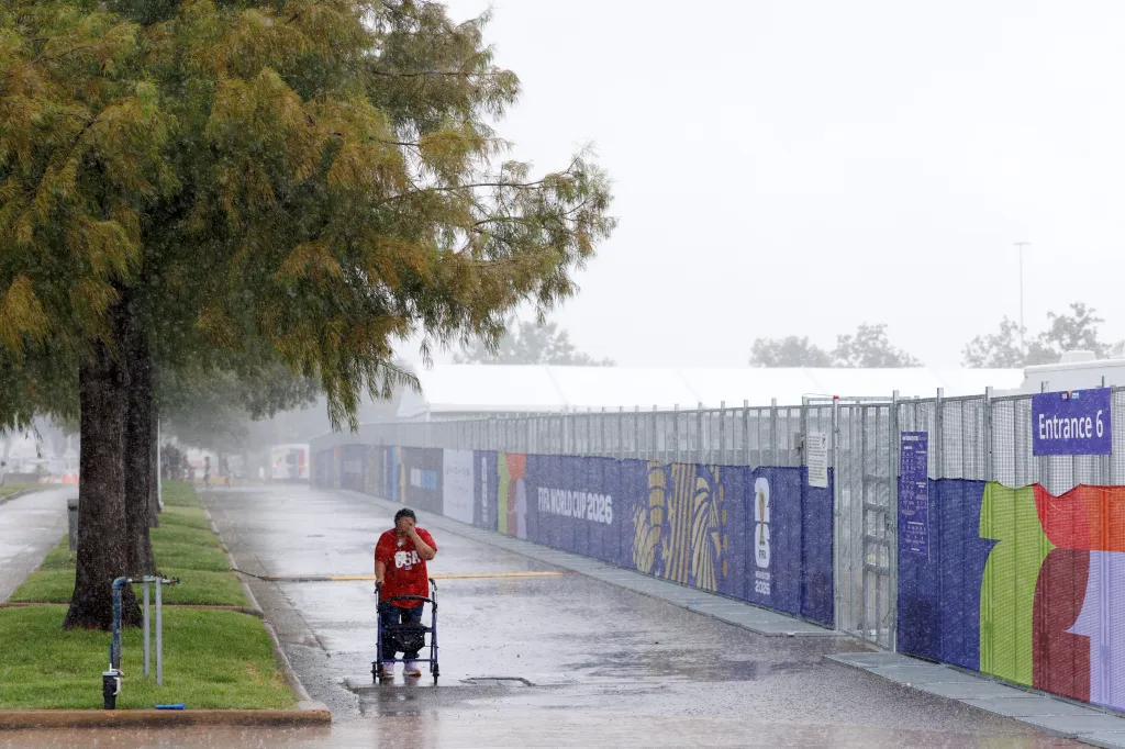 A fan walking in the rain with a walker outside the 2026 FIFA World Cup stadium.