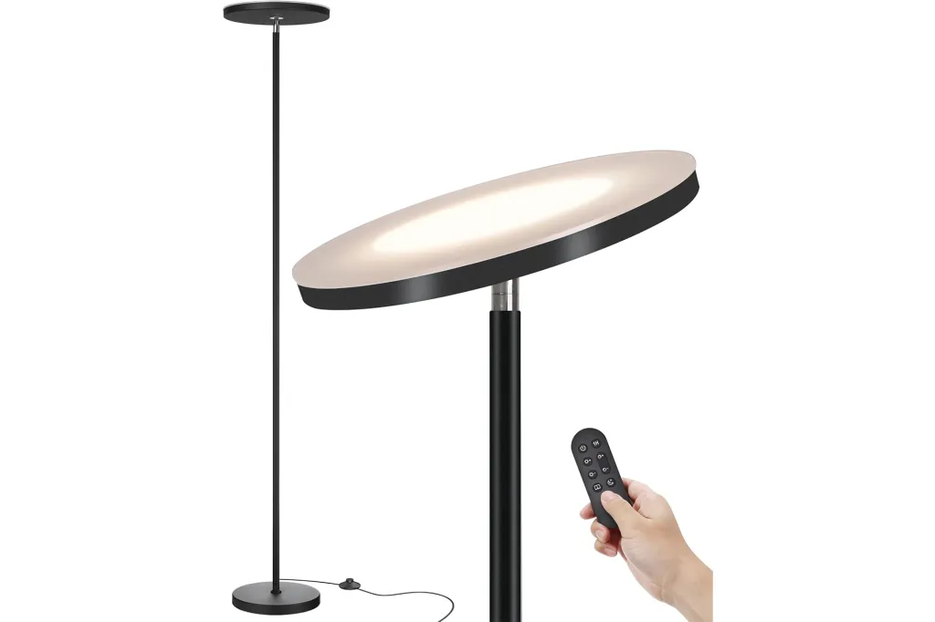 Black floor lamp with a circular flat light and a remote control being held.