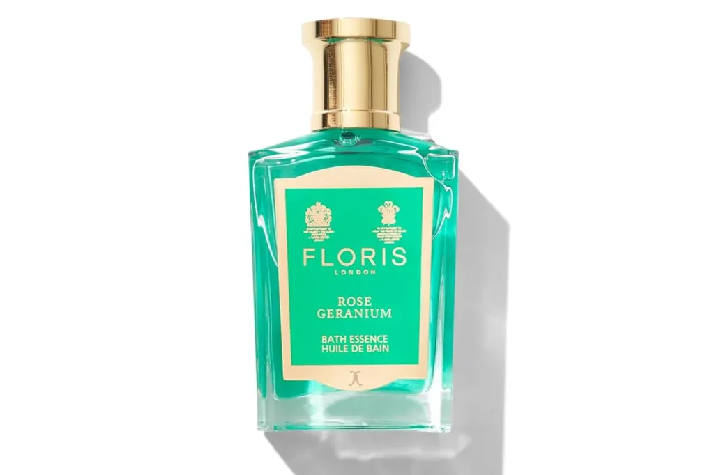 A bottle of Floris London Rose Geranium Bath Essence in a clear glass bottle with a gold top and green label.