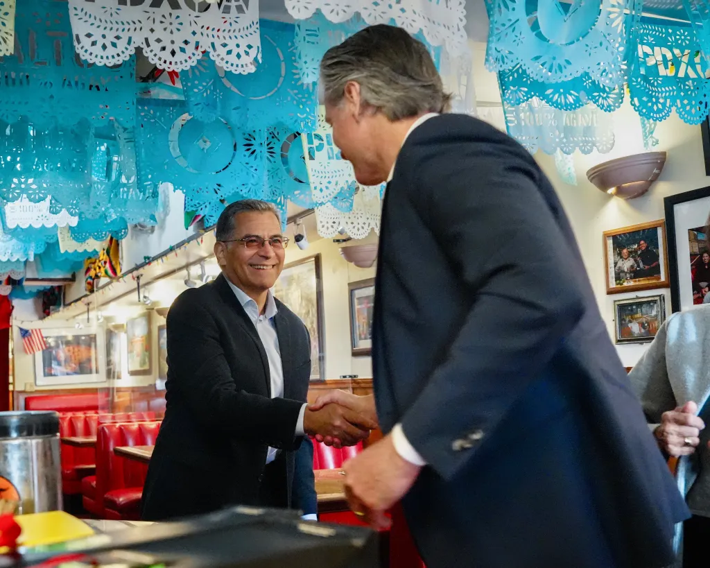 Gavin Newsom shaking hands with Xavier Becerra in a Mexican restaurant.