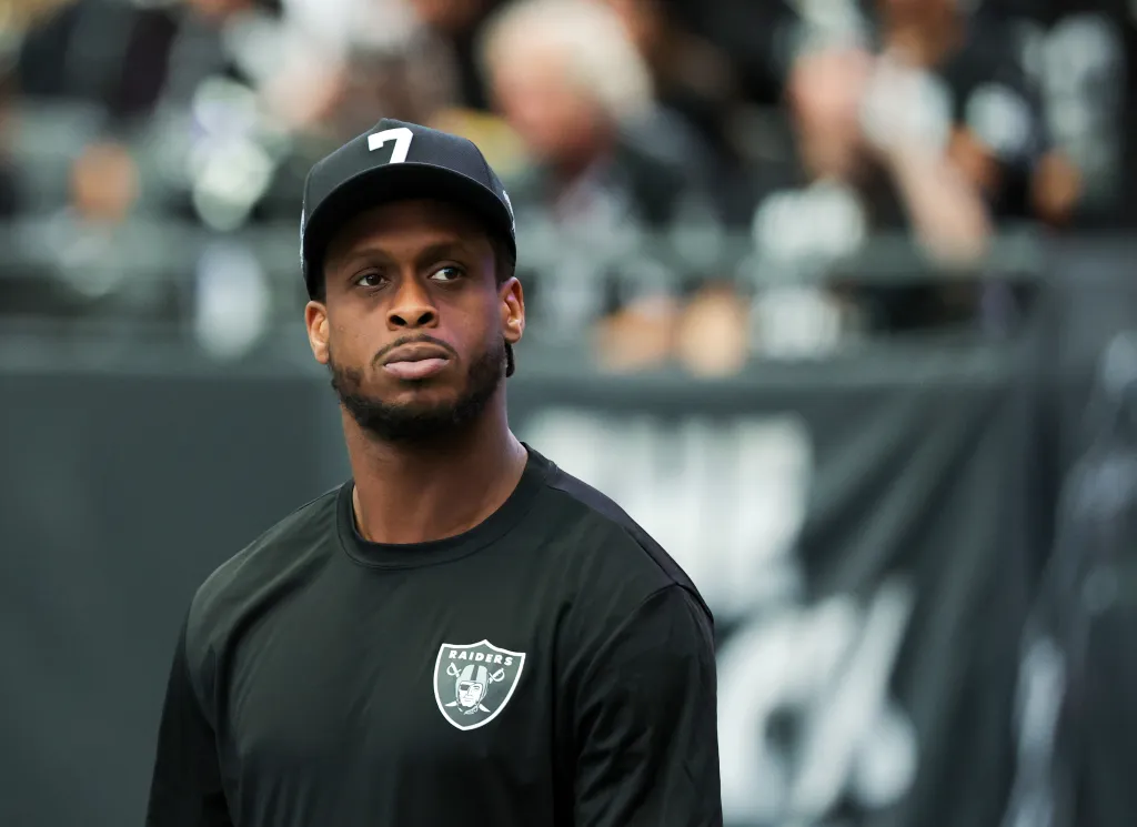 Geno Smith in a black shirt and cap with the number 7, standing on a football field.