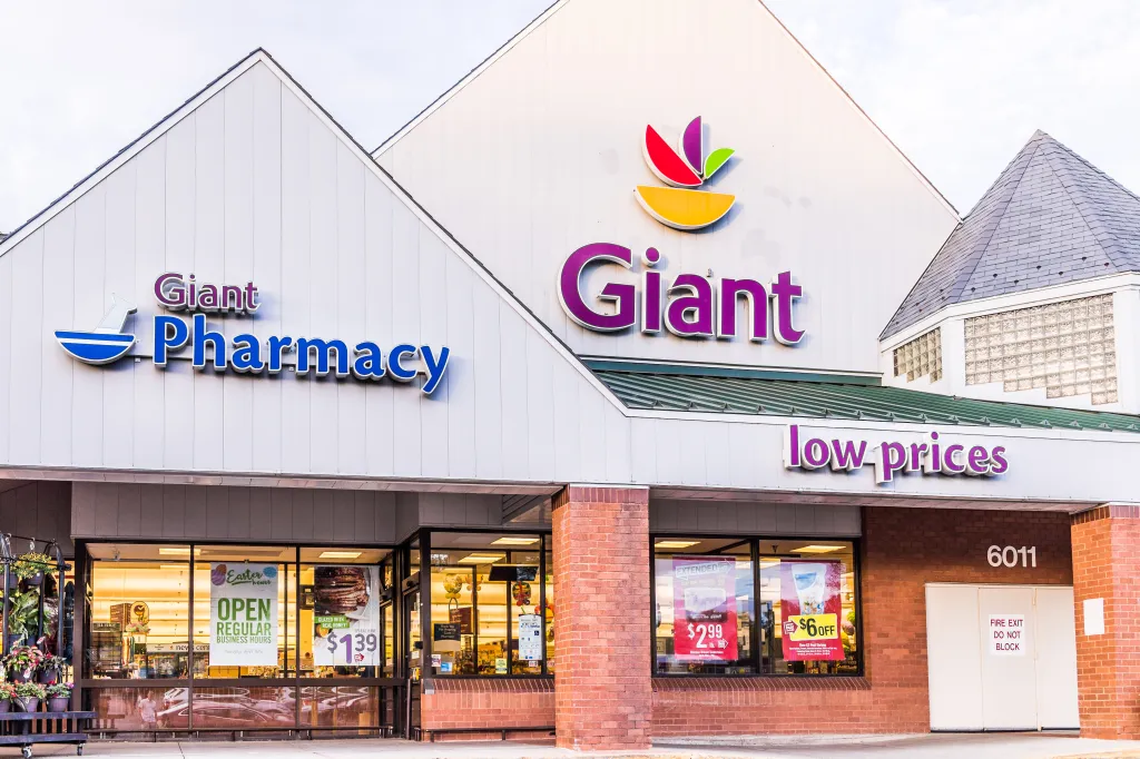 Exterior facade of a Giant grocery store and pharmacy, with "low prices" and promotional signs for ham, chicken, and shrimp visible through the windows.