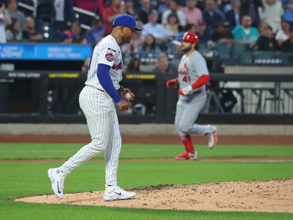 Mets pitcher Freddy Peralta (51) walking off the mound while Cardinals first baseman Alec Burleson (41) runs in the background.