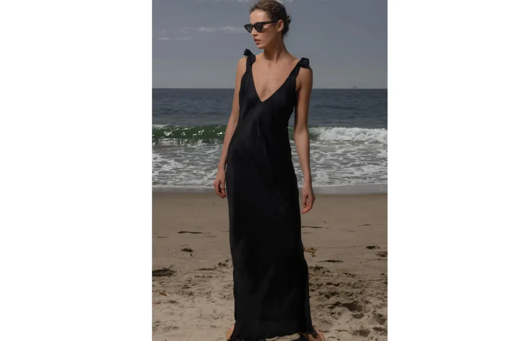 Woman in black maxi dress and sunglasses on a beach.