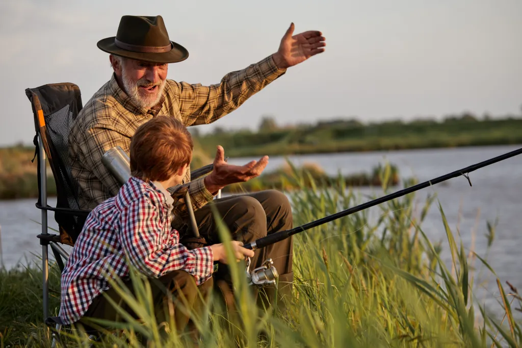 Grandfather in a hat teaches a boy to fish.