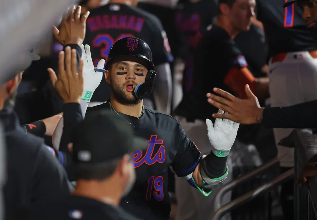 New York Mets shortstop Bo Bichette high-fives teammates in the dugout after scoring a solo home run.
