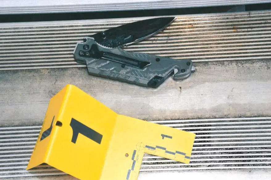 A black folding knife and a yellow evidence marker labeled "1" on a ribbed surface.