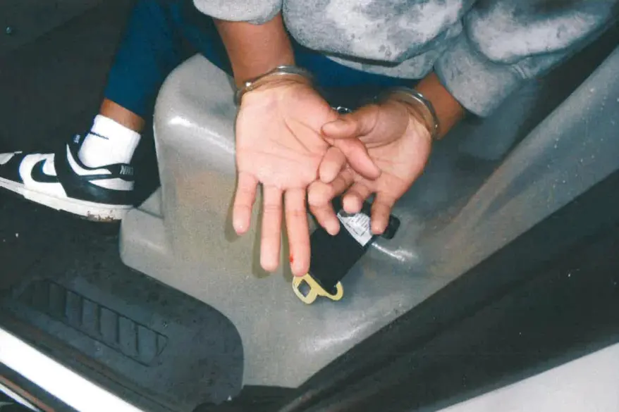A person's cuffed hands showing a bloody finger in a car.