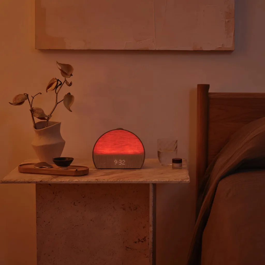 A Hatch Restore 2 sleep device sits on a bedside table, glowing red to display the time 9:32.