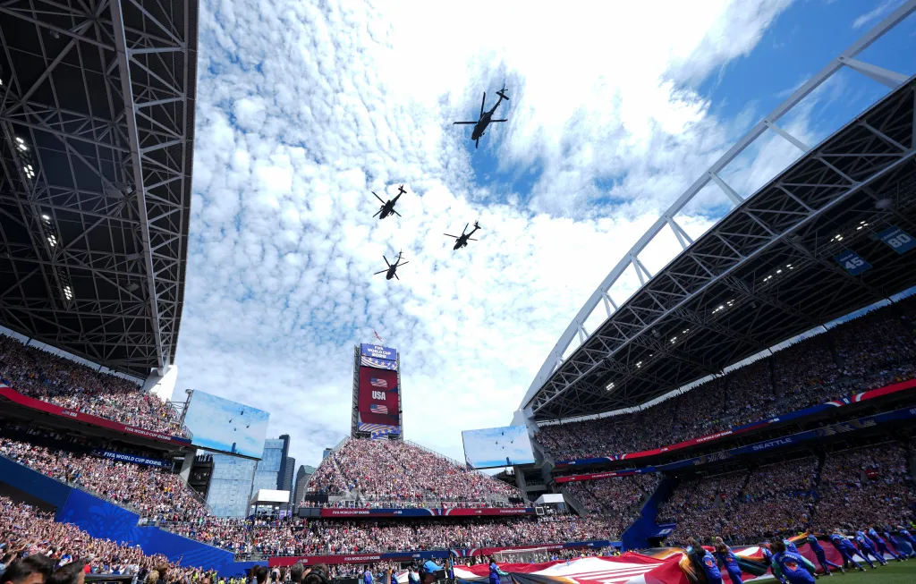 Four helicopters flying over Seattle Stadium with fans and "FIFA World Cup 2026" displayed on the screens.