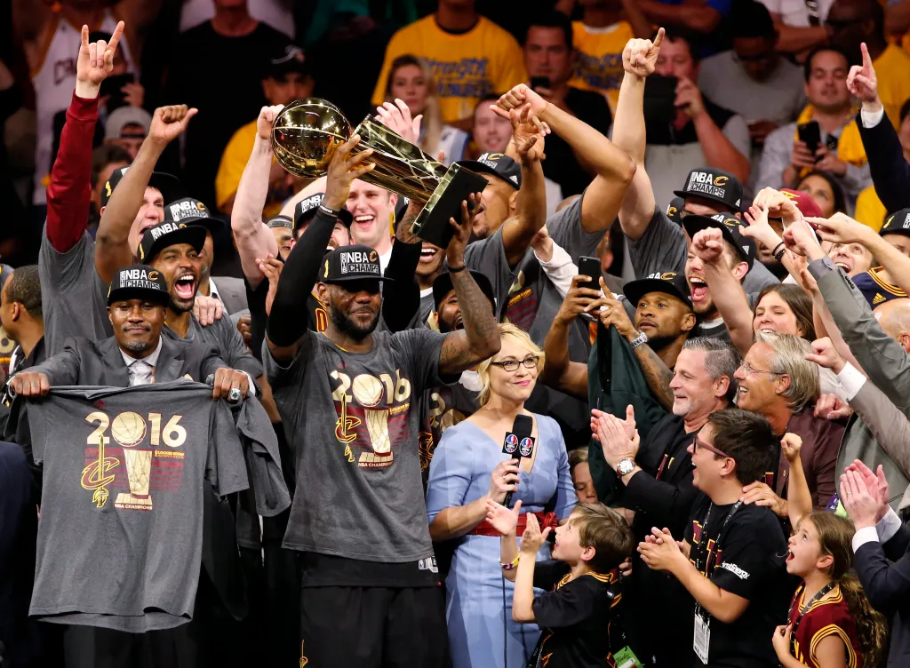 LeBron James holding up the Larry O'Brien Championship Trophy with his teammates after winning the NBA Finals.