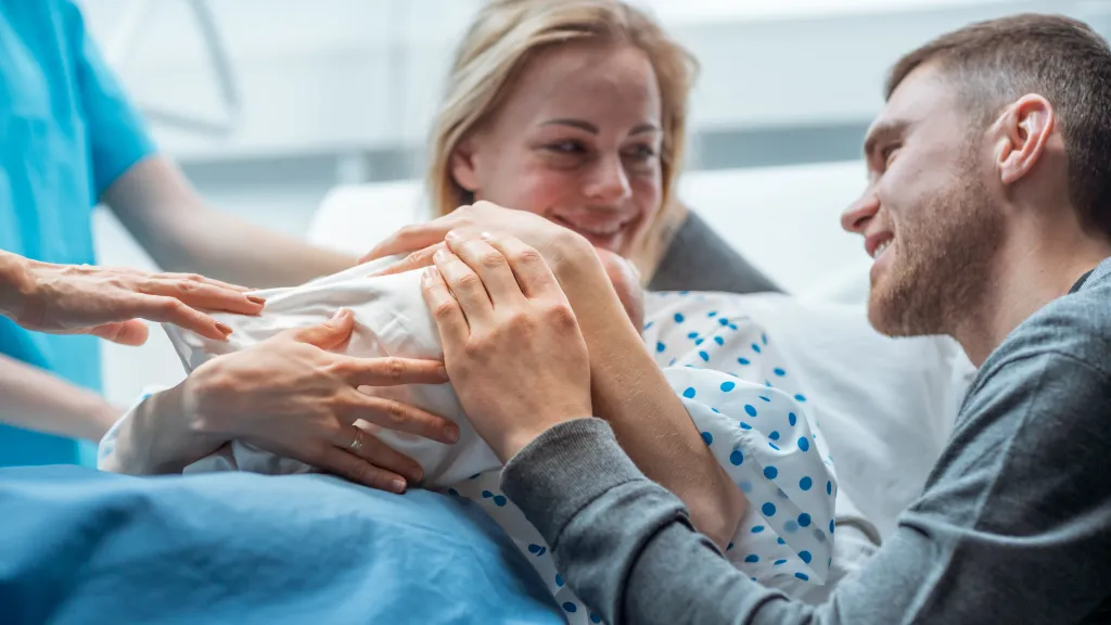 Midwife helping a mother hold her newborn as the father embraces them.