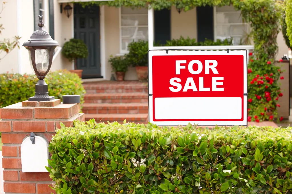 "For Sale" sign in front of a bungalow with a well-maintained garden.
