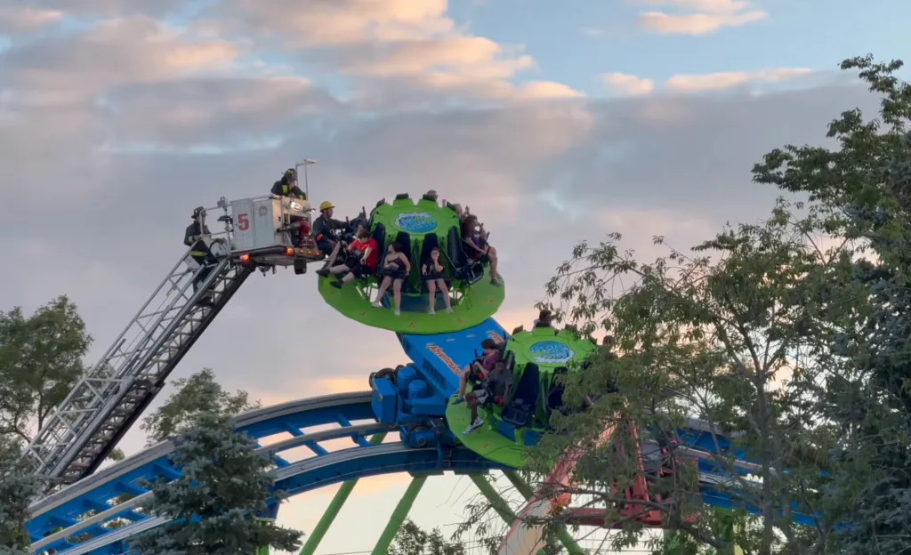 Firefighters on a ladder rescue people from a broken-down amusement park ride.