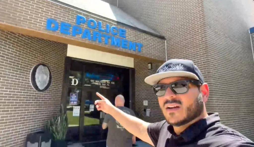 Independent journalist Sean Reyes aka The Long Island Auditor pointing to the entrance of a police department.