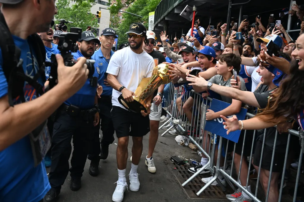 Jalen Brunson holds the Larry O'Brien Trophy closer to fans reaching out to touch it during a parade.