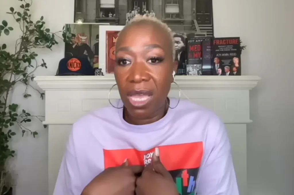 Joy Reid speaking with a serious expression, wearing a light purple shirt with a red and black graphic design.