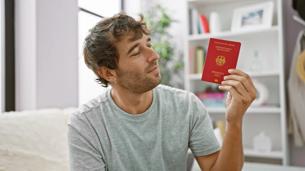 Man lounging on sofa holding German passport.