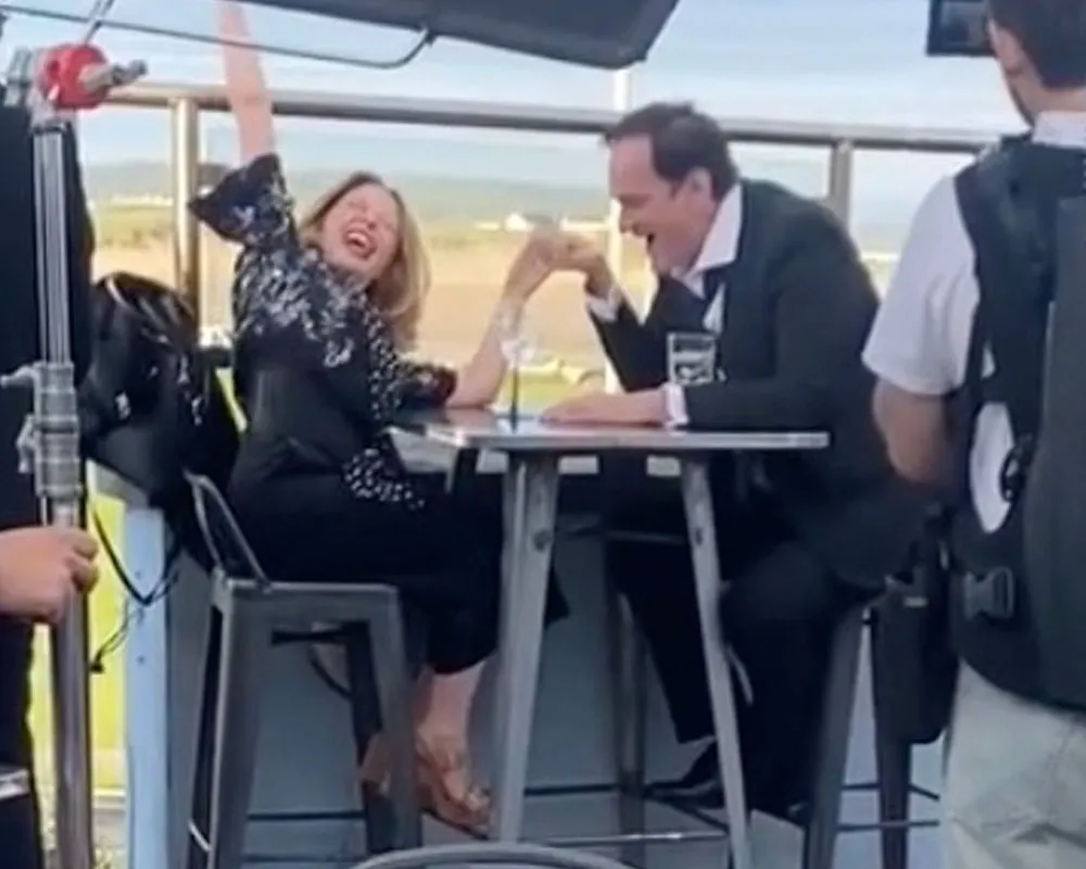 Kylie Minogue and Quentin Tarantino smiling and arm wrestling at a tall table.