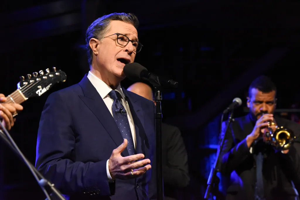 Stephen Colbert performing on stage with a band.
