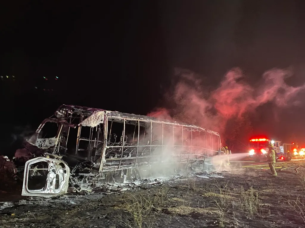Firefighters extinguish the burning remains of a bus following a fatal head-on collision.