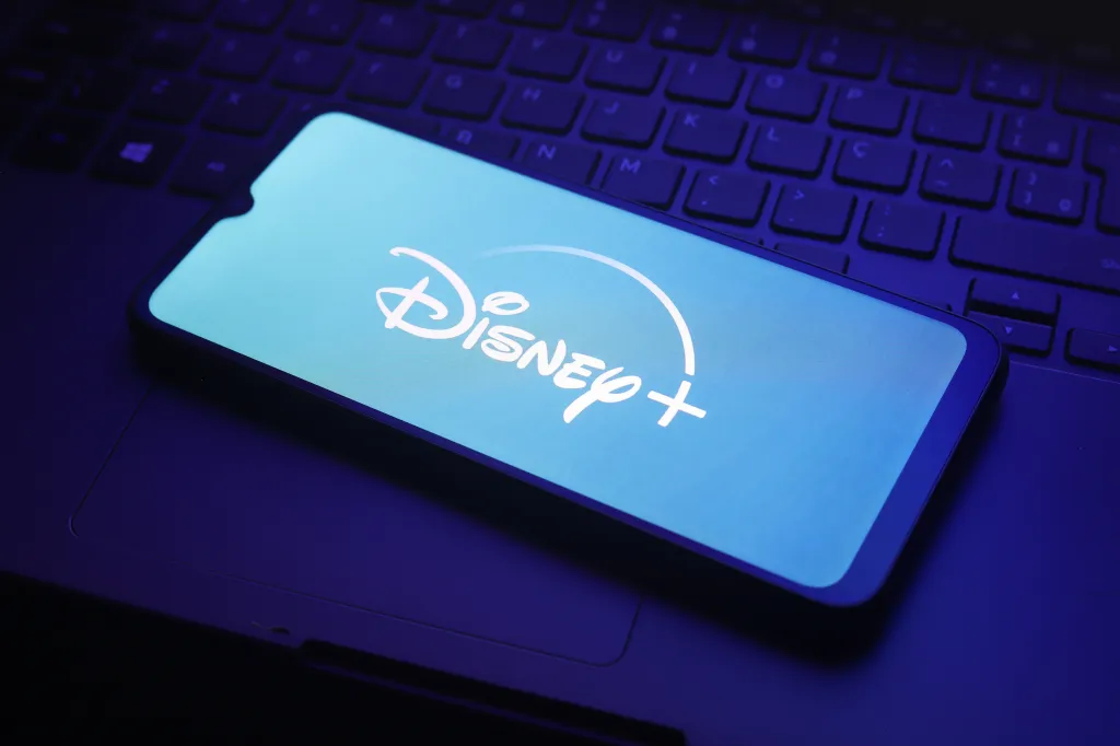 Illustration of the Disney+ logo displayed on a smartphone screen resting on a laptop keyboard.