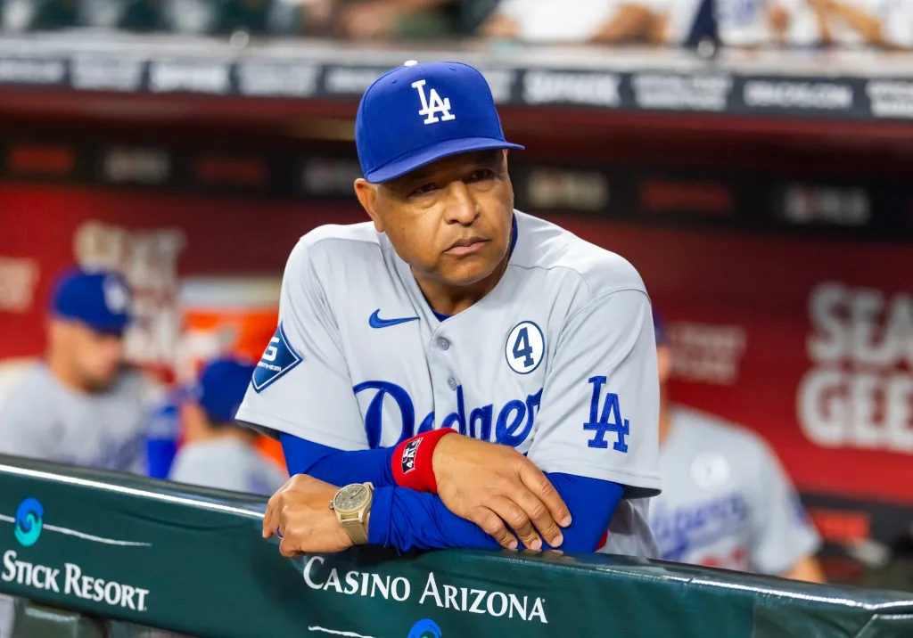 Dave Roberts, manager for the Los Angeles Dodgers, leaning against a dugout railing during a game against the Arizona Diamondbacks.