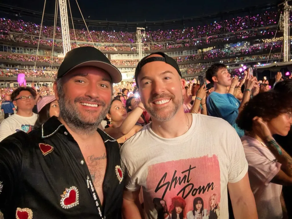 Two men smiling at a concert with a large crowd in the background.