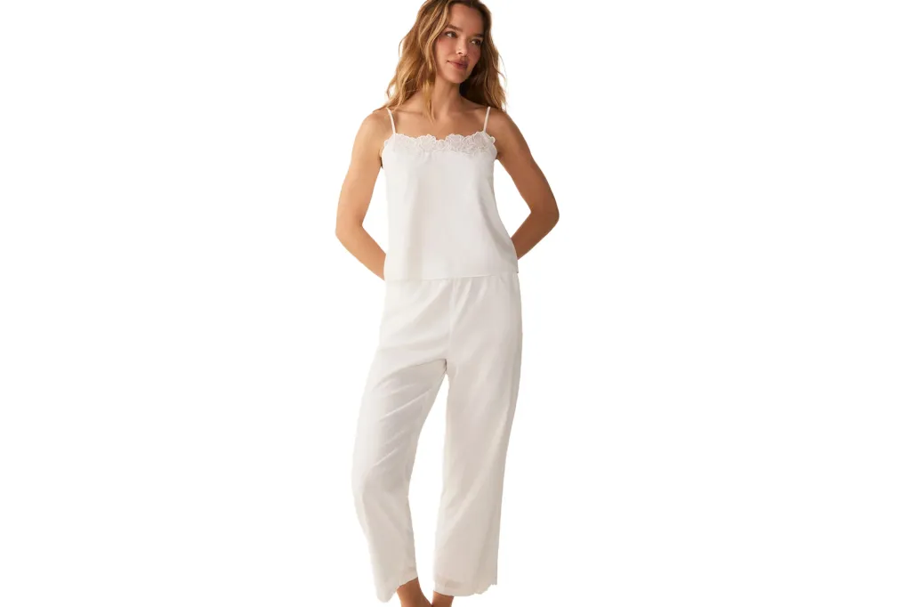 A woman wearing white pajama pants and a white camisole with lace trim.