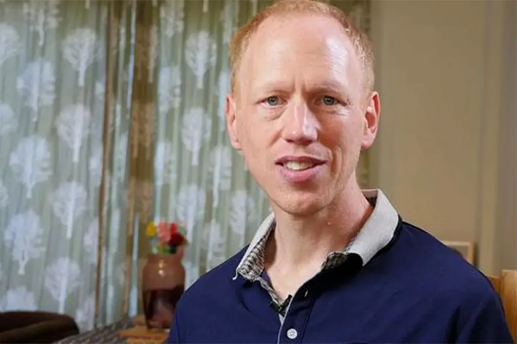 Luke Salmons, a man with light red hair and a navy polo shirt, speaking while looking at the camera.