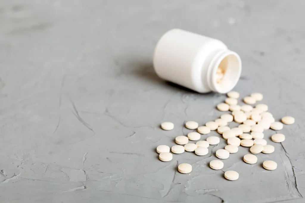 White pills spilled out of a white medicine bottle on a gray background.