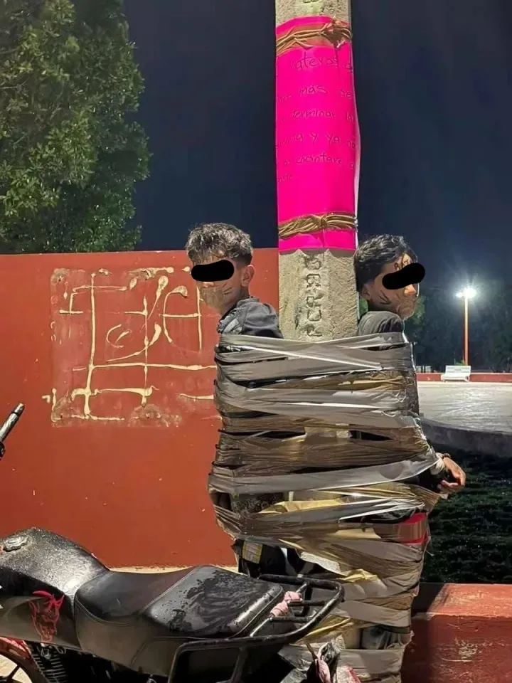 Two men taped to a lamppost next to a motorcycle.