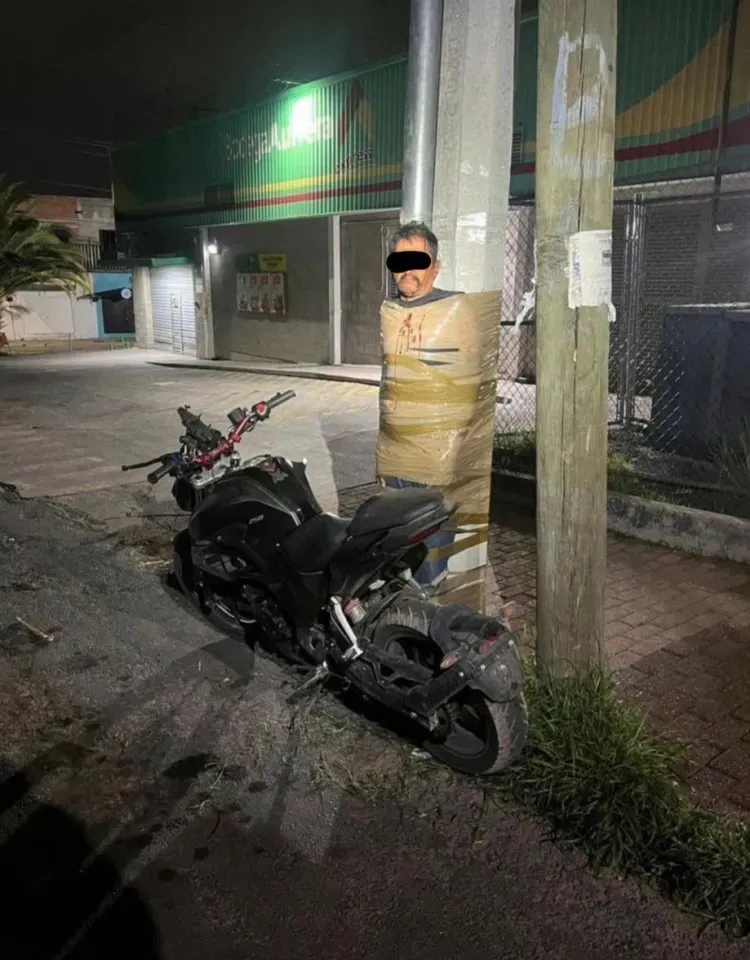 Man taped to a lamppost next to a motorcycle.