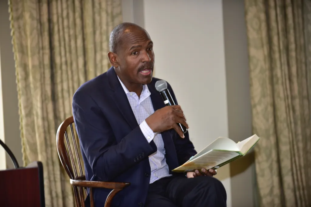 Jimmie James speaking into a microphone while holding a book at the Milken Institute.